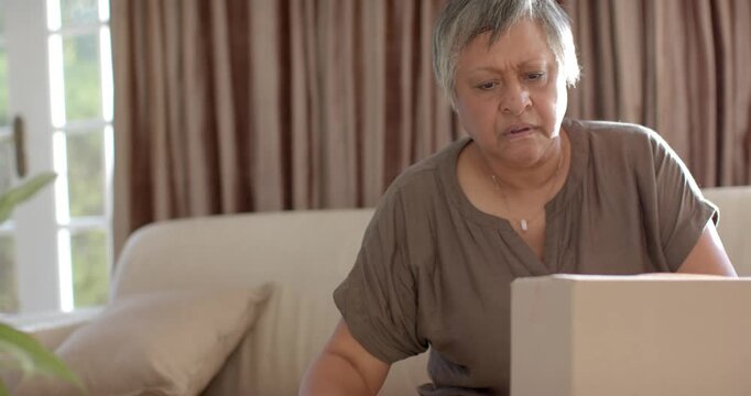 Senior African American woman after checking phone peeling tape, opening box on sofa checking items