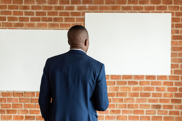 Person in a suit facing blank canvases on a brick wall.