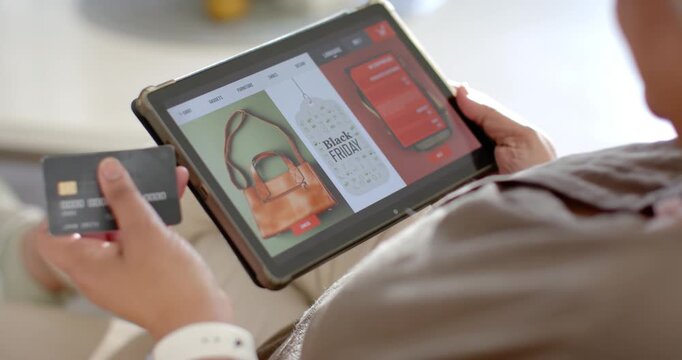 Mature African woman on couch wearing white band seeing Black Friday on tablet checking credit card