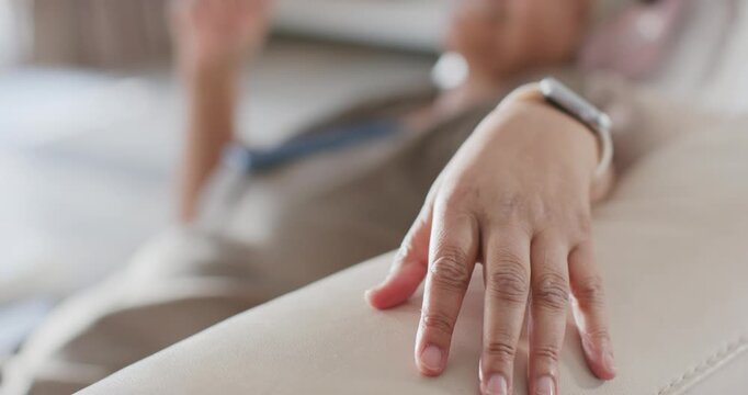 Woman resting right wrist on sofa armrest at home, smartwatch on wrist, left hand checking device