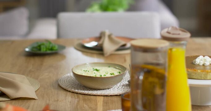 Camera is sliding, showing ceramic bowl of creamy soup; spoon is settling by bowl, preparing meal