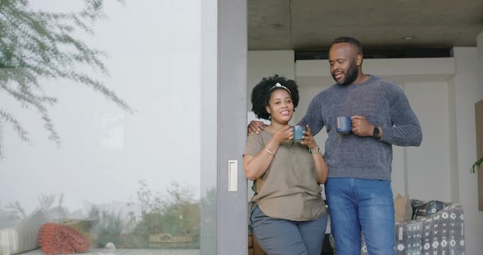 African American couple standing in sliding door holding dark ceramic mugs after moving, laughing