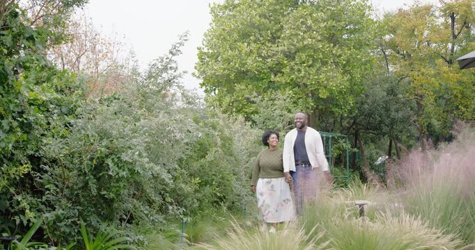 African couple entering backyard from green gate, walking path, holding hands, sharing moment