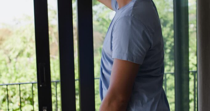 African American man in blue shirt by door shading eyes from sun viewing balcony, copy space