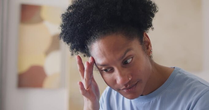 Adult African American woman raising hand, smoothing eyebrow while peering into mirror at vanity
