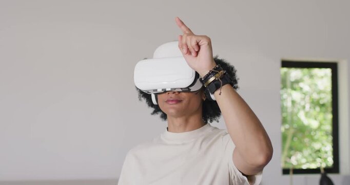 African American man tapping VR headset then gesturing to manipulate VR objects at home near window