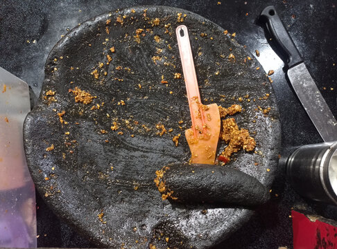 Top view of a traditional Indonesian large black stone mortar (cobek) with leftover spicy peanut sauce and a small plastic spatula.