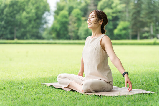 Asian women taking deep breaths, stretching, and doing yoga in a park.