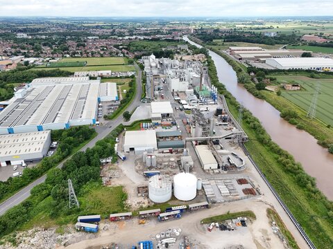 Aerial view of an industrial facility with storage tanks, warehouses, and a river flowing through the landscape, England, United Kingdom.