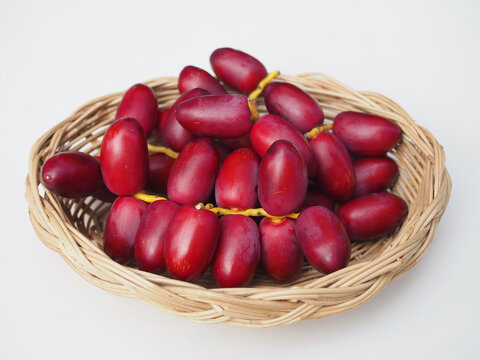 Fresh, red dates are arranged in a wicker basket on a white surface. They look appetizing and delicious.
