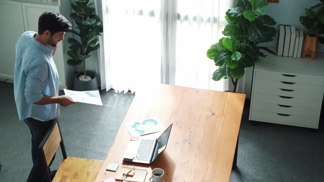 Relaxed caucasian businessman talking phone with team while sitting on table. Smart manager speaking and calling with colleague about marketing strategy while looking at financial graph. Convocation.
