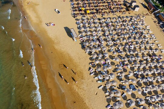 Aerial view of Kilyos shore with rows of parasols on the sandy beach and people walking along the water in Sariyer, Istanbul, Turkey.