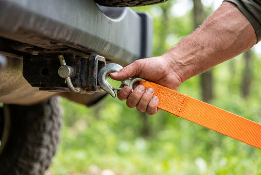 Male hand attaching orange tow strap to vehicle hitch receiver outdoors