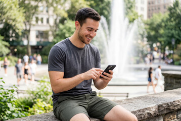 Obraz premium Happy man using smartphone in city park near water fountain