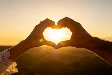 Man and woman hands framing sun in heart shape against blue sky, couple in love, romance and hopeful bright future concept © Yan