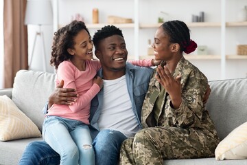 Obraz premium Happy Smiling African American Woman In Military Uniform Engaging With Two Young Daughters At Home, Creating Joyful Family Moment In Living Room, Celebrating Togetherness And Love.