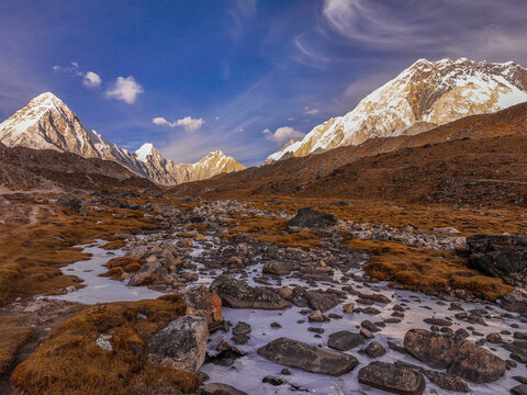 Aerial view of Everest Base Camp featuring snow-capped Himalayan peaks, a rocky stream bed with icy patches, and brown alpine tundra in Khumjung, Koshi Province, Nepal.