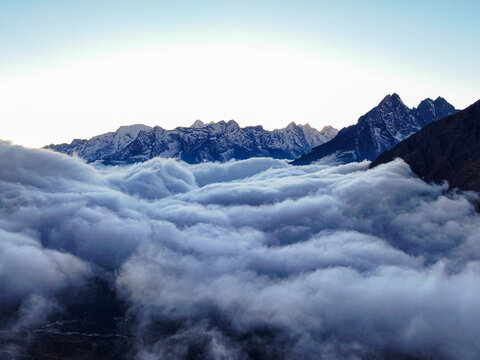 Aerial view of the Himalayan mountain range rising above a thick sea of clouds with snow-capped peaks illuminated by soft morning light in Khumjung, Koshi Province, Nepal.