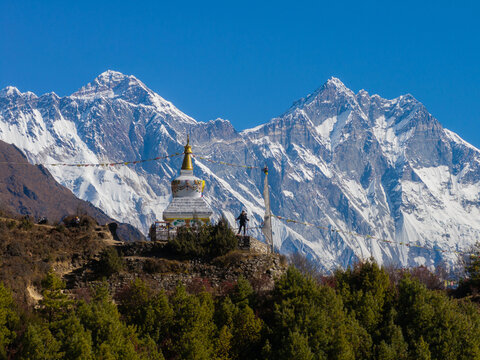 Aerial view of a Buddhist stupa set against the snow-capped peaks of the Himalayas with prayer flags fluttering in the clear blue sky in Nepal.