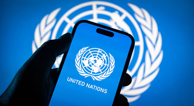 Closeup of a hand holding a smartphone displaying the united nations logo against a blurred un flag background