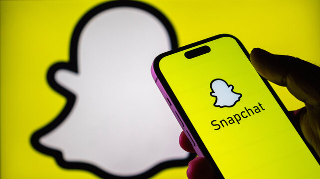 Hand holding a smartphone displaying the snapchat logo on a yellow background