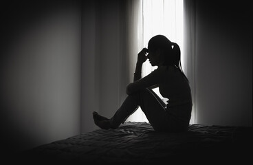 Depressed woman sitting alone in a dark room, representing domestic violence, emotional abuse, trauma, anxiety, loneliness, fear, and mental health struggles.