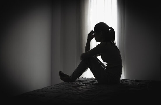 Depressed woman sitting alone in a dark room, representing domestic violence, emotional abuse, trauma, anxiety, loneliness, fear, and mental health struggles.