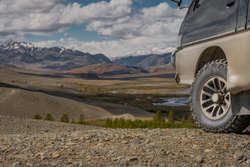 Side view of offroad camper van wheel parked on rocky hill over vast valley. Expedition 4x4 car tire traveling through remote scenic mountain wilderness under cloudy sky. © ANDREY