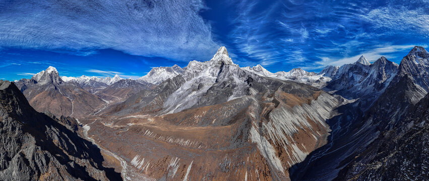 Aerial view of Ama Dablam peak rising above the rugged, snow-covered Himalayan mountain range with deep valleys and a clear blue sky in Nepal.
