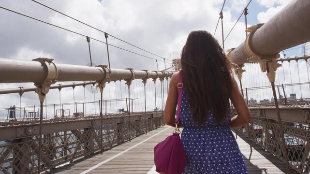 New York City Woman. Young woman portrait on Brooklyn bridge, New York city NYC, Manhattan, USA. Walking tourist in blue dress doing summer travel by landmark. SLOW MOTION