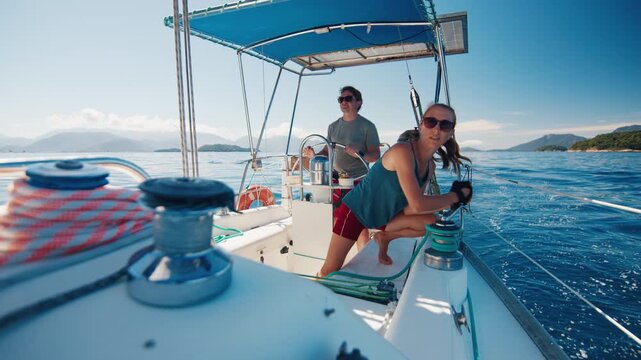 Sailing in the smooth sea during sunny day. Man and woman sail the small sailing boat in the region of the island of Ilha Grande in Brazil