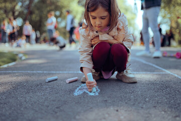 Young Girl Drawing Chalk Heart On Asphalt At Park Event. Little child creating colourful street art during lively community summer festival outdoors © nicoletaionescu