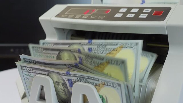 Close up jib shot, electronic money counting machine with digital display processing 100 Dollar bills, soft focus, slow motion