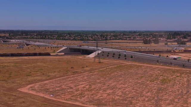 Reversing Aerial Drone Shot Above Dirt Field Revealing Overpass Train Power Lines and Farmland Beyond