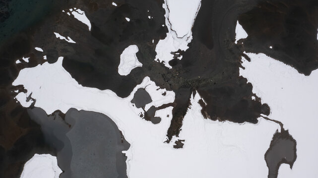 Aerial view of the snow-covered water near Babusar Pass with dark rocky terrain and patches of ice in lulusar lake Babusar, KPK, Pakistan.
