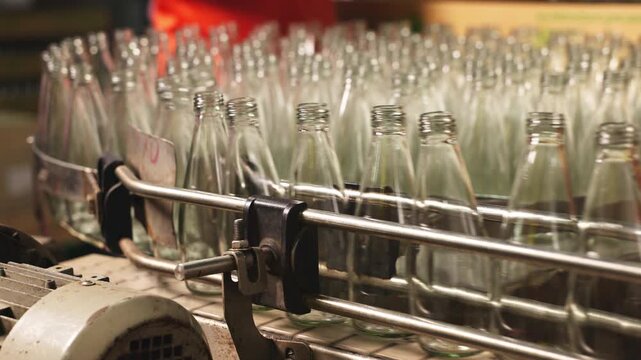 Close-up of industrial bottling equipment precisely filling glass containers with liquid during high-speed beverage production process in factory