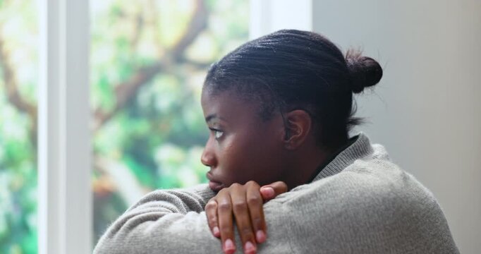 Black woman, window and overthinking in home for mistake, anxiety or fear with self doubt or regret. Trauma, worry or person with depression in living room with stress for mental health or burnout