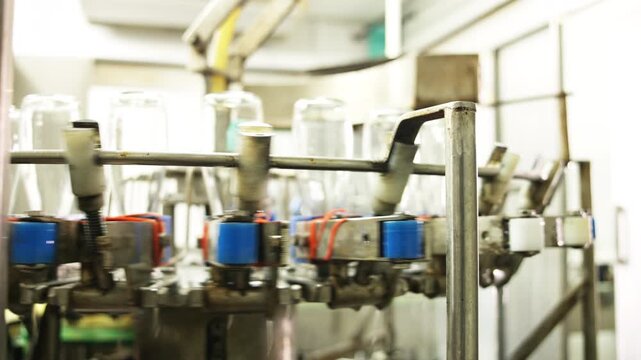 Close-up of industrial bottling equipment precisely filling glass containers with liquid during high-speed beverage production process in factory