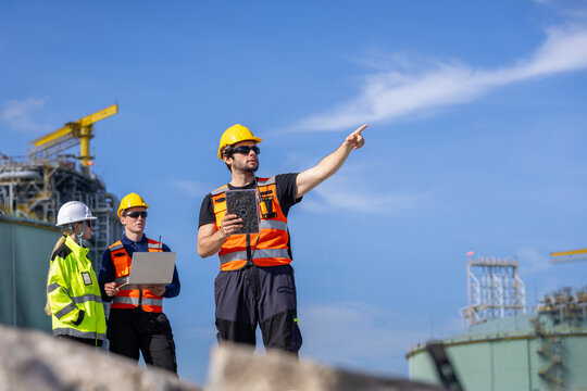 Team of industrial workers checking data at natural gas plant, Engineers working with laptop and radio at LNG storage facility, Professional technical team analyzing project at gas infrastructure site