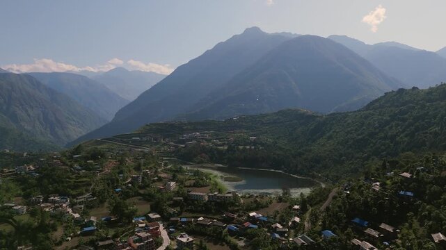 Wide cinematic drone shot of a rural mountain town nestled in a deep valley basin below high peaks