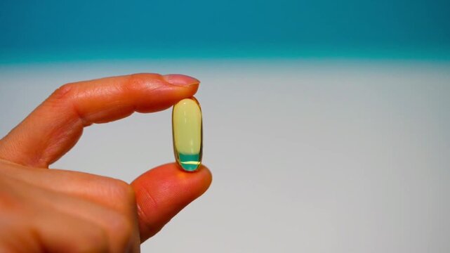Hand of woman, girl holds golden capsule with Omega 3 on light background. Vitamins