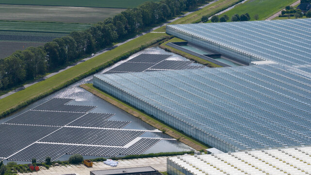 Aerial view of a large greenhouse complex featuring a floating solar panel array on a pond in Middenmeer, North Holland, Netherlands.