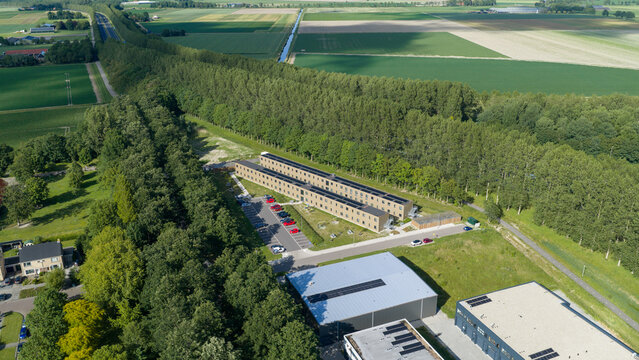 Aerial view of a modern residential building complex surrounded by lush green trees and agricultural fields in Middenmeer, North Holland, Netherlands.