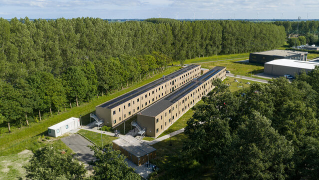 Aerial view of modular housing units surrounded by lush green trees and open fields in Middenmeer, North Holland, Netherlands.