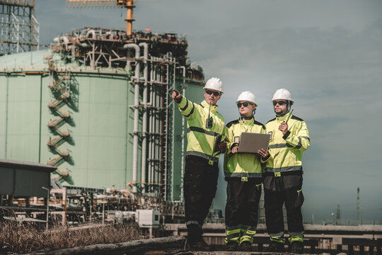 Industrial site workers in safety gear discussing project with laptop outdoor