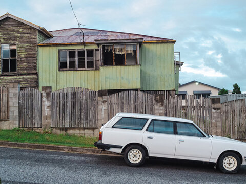 Weathered two‑storey house with station wagon outside