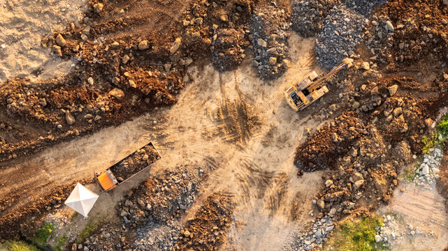 Aerial view of an excavator and a truck working on a construction site with piles of earth and rocks in Indonesia.