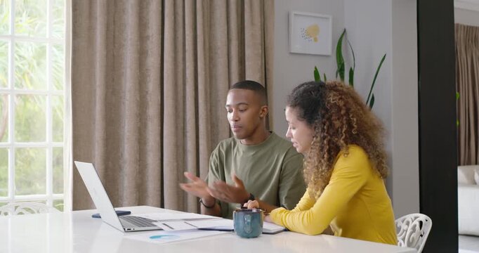 Couple sitting at dining table checking papers and laptop, reviewing, pointing, finalizing notes