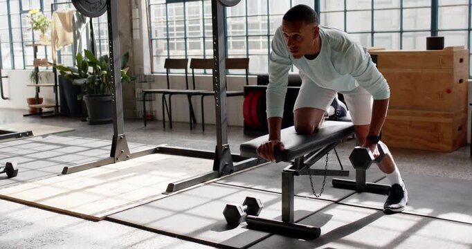 African American man reaching for dumbbell and rowing on bench for strength, copy space
