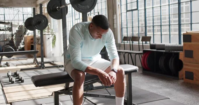 African American man pausing between sets on flat bench at gym, checking watch, gazing at barbell